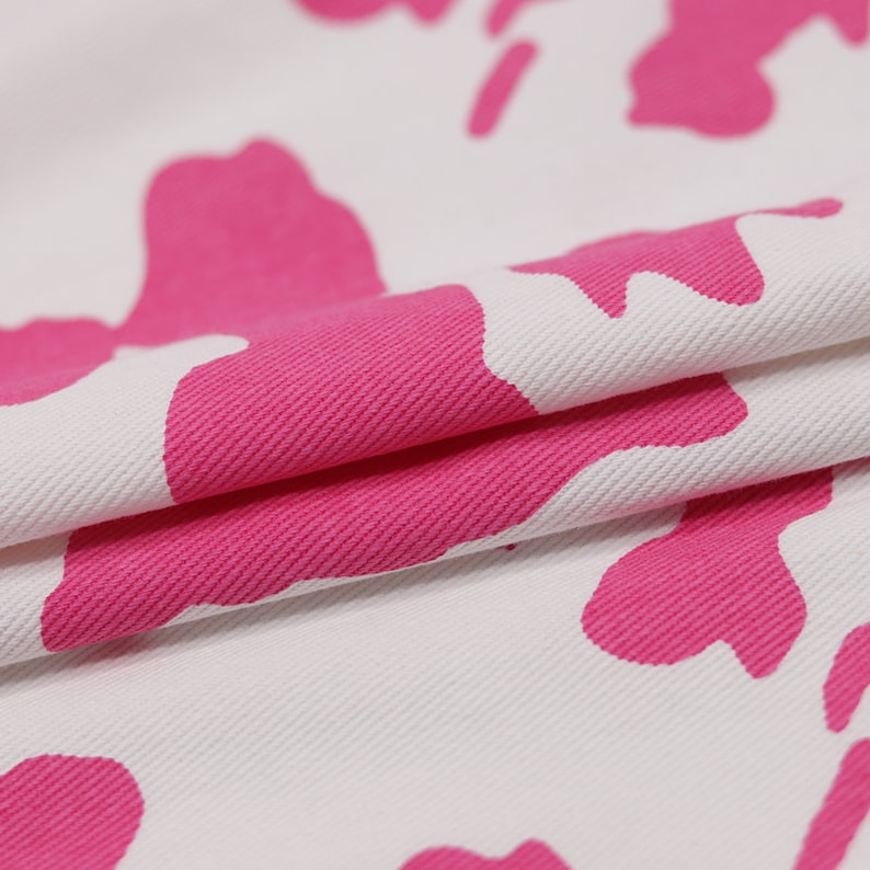 May include: White fabric with a pink abstract floral pattern. The fabric is folded over, showing the texture of the material.