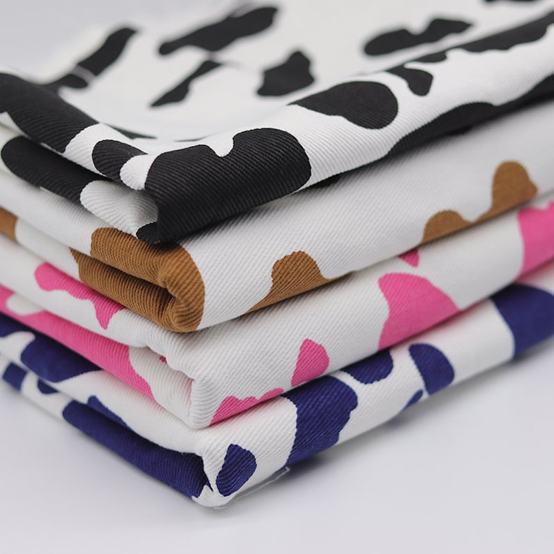 May include: Four pieces of white fabric with different colored abstract patterns. The fabric is folded in a stack, with the black pattern on top and the navy blue pattern on the bottom.