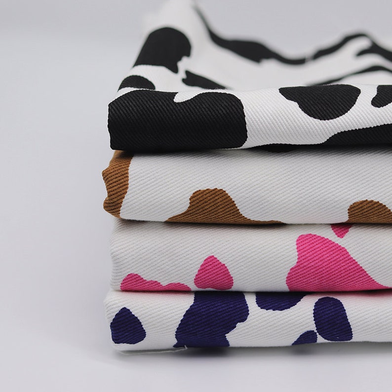 May include: Four pieces of fabric with a cow print pattern in different colors. The fabric is white with black, brown, pink, and purple spots.