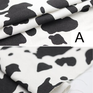 May include: Close-up of white fabric with a black cow print pattern. The fabric is folded over, showing the texture of the material.