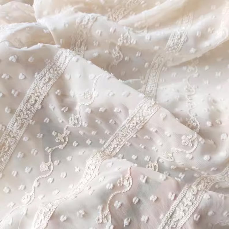 May include: White sheer fabric with a delicate embroidered pattern and small raised dots. The fabric has a soft, airy feel.