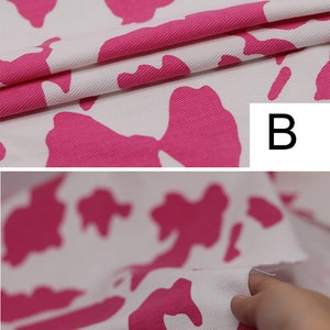May include: Pink and white cow print fabric with a textured surface. The fabric is folded over and the letter "B" is visible in the upper right corner.