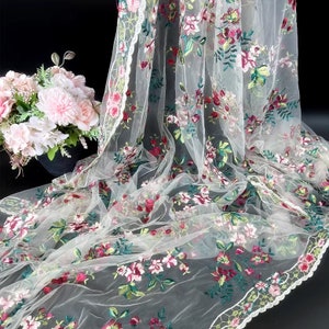 May include: White tulle fabric with embroidered floral designs in shades of pink, green, and red. The fabric has a delicate lace trim.