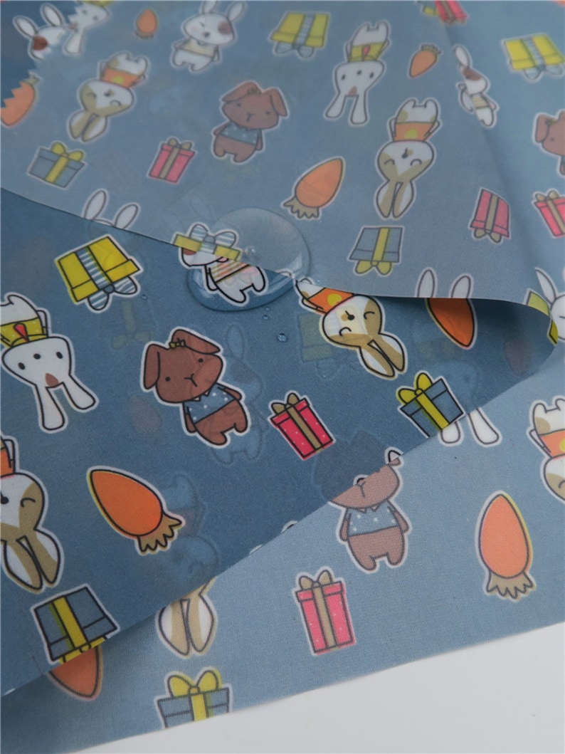 May include: Blue fabric with a repeating pattern of cartoon animals, including rabbits, dogs, and carrots. The fabric is waterproof and has a subtle sheen.