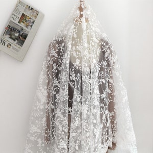 May include: White floral embroidered tulle fabric. The fabric is sheer and delicate with a delicate floral pattern.