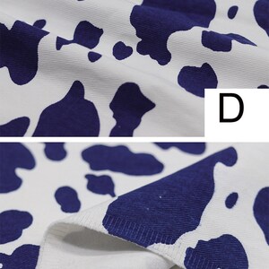 May include: Close-up of white fabric with a blue cow print pattern. The fabric is textured and has a slight sheen. The fabric is folded in half, showing the inside of the fabric.