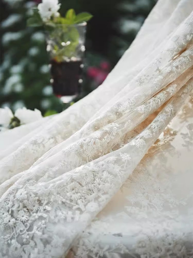 Op de afbeelding: Wit kant met een delicaat bloemenpatroon. De stof is zacht en doorschijnend en heeft een romantische en elegante uitstraling.