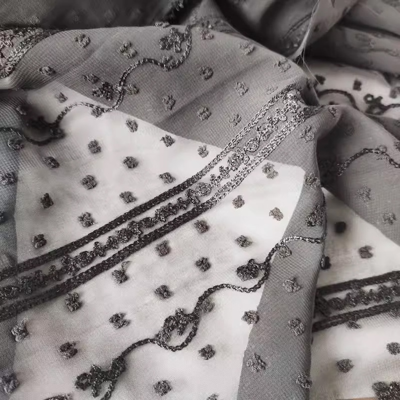 May include: Black and white sheer fabric with a repeating pattern of small dots and a larger, more intricate design. The fabric has a delicate, almost lace-like quality.