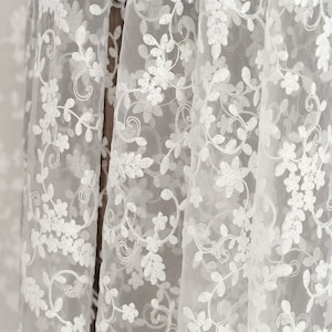 May include: White sheer fabric with a delicate floral embroidery pattern. The fabric is lightweight and translucent, with a soft, flowing texture.