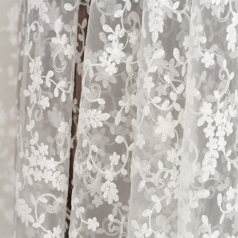 May include: White sheer fabric with a delicate floral embroidery pattern. The fabric is lightweight and translucent, with a soft, flowing texture.