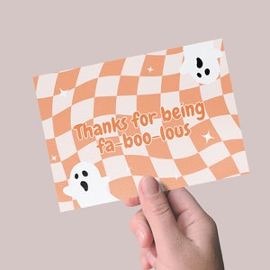 May include: A card with a checkered orange and white background. The card has two white ghosts and the text "Thanks for being fa-boo-lous".