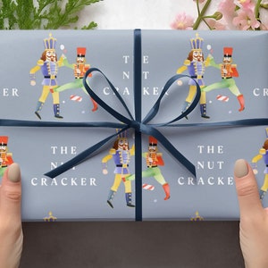 May include: A blue gift box with a navy blue ribbon. The box is wrapped in paper with a repeating pattern of nutcracker soldiers. The text "The Nutcracker" is printed on the box.