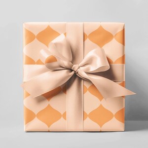 Könnte beinhalten: Ein verpacktes Geschenk mit pfirsichfarbenem Geschenkpapier mit einem orangefarbenen geometrischen Muster. Ein passendes pfirsichfarbenes Satinband ist zu einer Schleife um die Schachtel gebunden, was eine dekorative und elegante Präsentation ergibt.