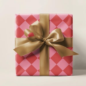 May include: A wrapped gift box with pink and red diamond patterned wrapping paper. A gold satin ribbon is tied around the box in a bow. The gift is ready to be given.