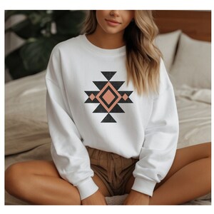 May include: White sweatshirt featuring a geometric design in black and peach. The design incorporates a large diamond shape with smaller triangles surrounding it.