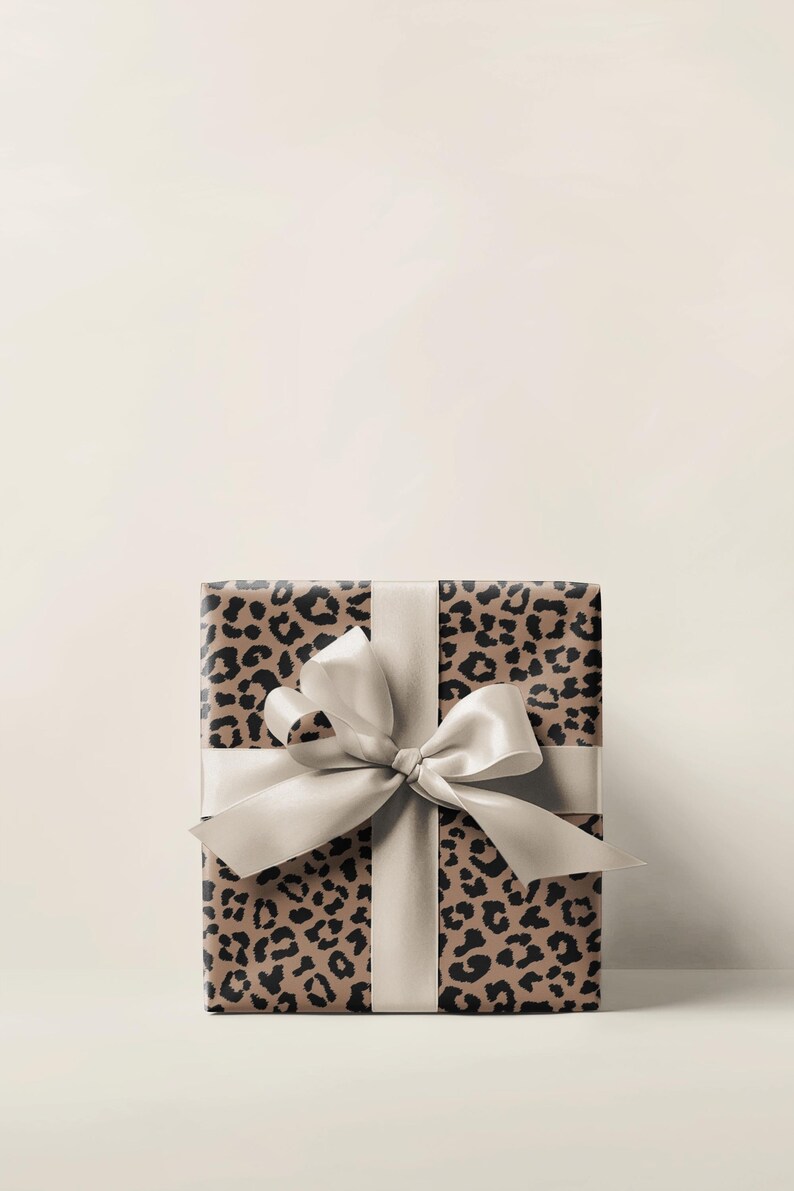 May include: A wrapped gift box featuring a leopard print design in shades of brown and black. The box is tied with a wide, light-colored satin ribbon and bow. The overall aesthetic is elegant and suitable for various occasions.