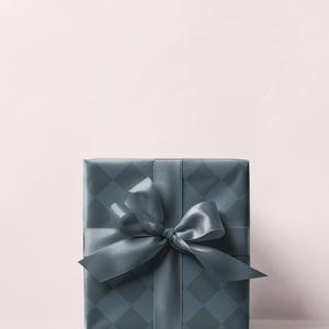 May include: A square gift box wrapped in teal paper with a diamond pattern. A matching teal satin ribbon is tied in a bow on top. The background is a soft pink.