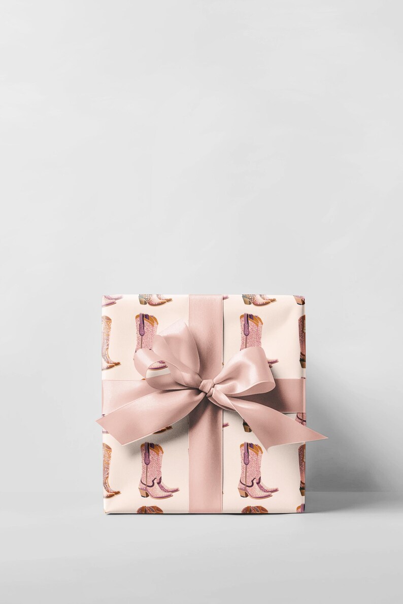 Pu&ograve; includere: Una scatola regalo avvolta in carta da regalo rosa e bianca con un fiocco rosa. La carta da regalo ha un motivo di stivali da cowboy rosa.
