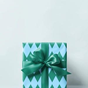 May include: A wrapped gift box with a light blue and green diamond pattern. The box is tied with a green satin ribbon and bow. The background is a solid, light blue color.