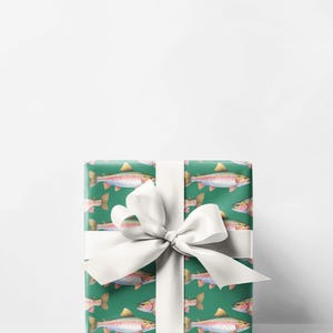 May include: A wrapped gift with green wrapping paper featuring a pattern of watercolor trout. The gift is tied with a white satin ribbon and bow. The trout are pink, yellow, and orange.