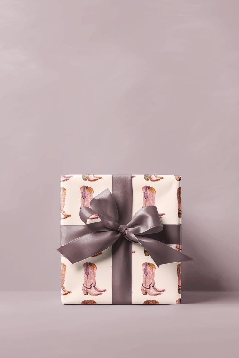 Pu&ograve; includere: Una scatola regalo avvolta in carta bianca con un motivo di stivali da cowboy rosa. La scatola &egrave; legata con un nastro di raso grigio.