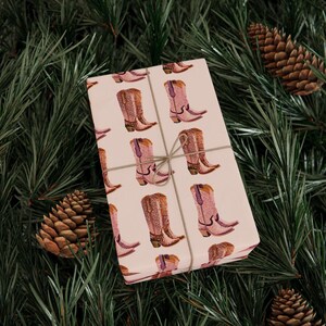 Pu&ograve; includere: Carta da regalo rosa con un motivo ripetitivo di stivali da cowboy rosa con strass. Il regalo &egrave; avvolto con spago.