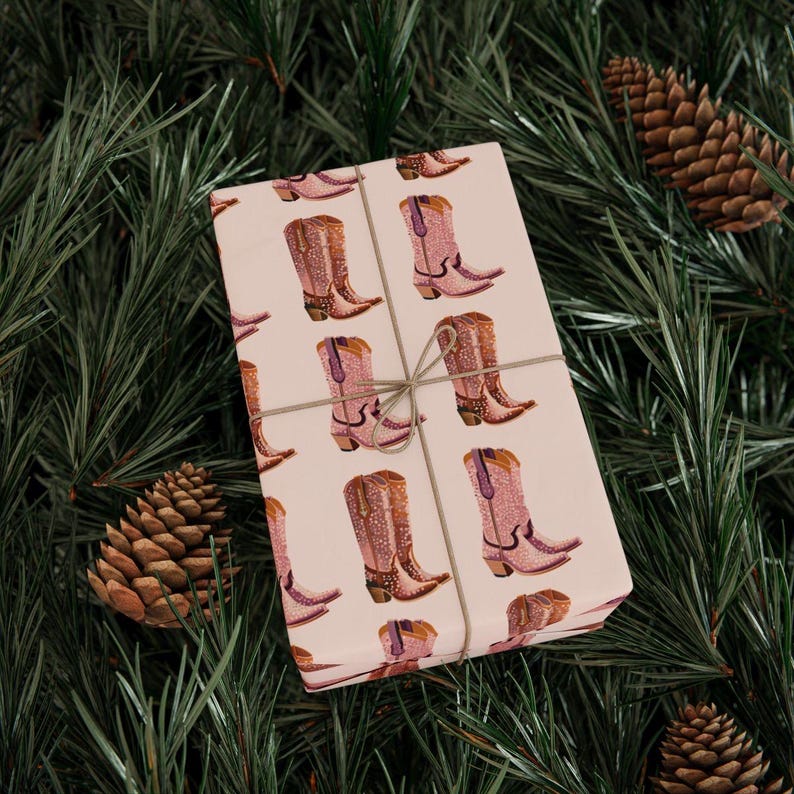 Pu&ograve; includere: Carta da regalo rosa con un motivo ripetitivo di stivali da cowboy rosa con strass. Il regalo &egrave; avvolto con spago.