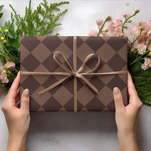Op de afbeelding: Een bruine en beige cadeaudoos met een ruitpatroon is vastgebonden met een bruin lint. De doos wordt vastgehouden door twee handen.