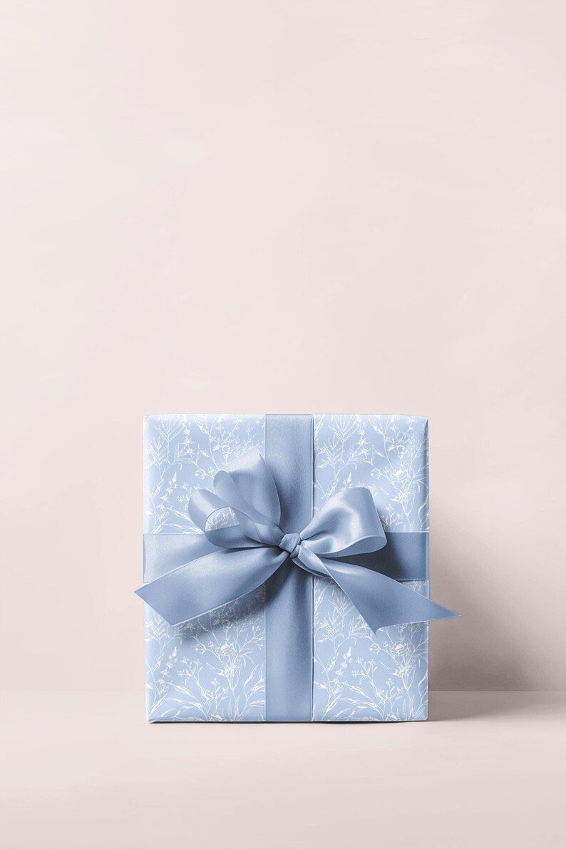 Puede incluir: Una caja de regalo azul claro con un patr&oacute;n floral blanco y una cinta de sat&eacute;n azul a juego atada en un lazo.