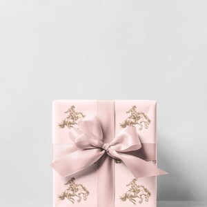 May include: A wrapped gift box with a light pink background and a matching ribbon tied in a bow. The wrapping paper features a repeating pattern of a cowboy riding a horse in a gold color.