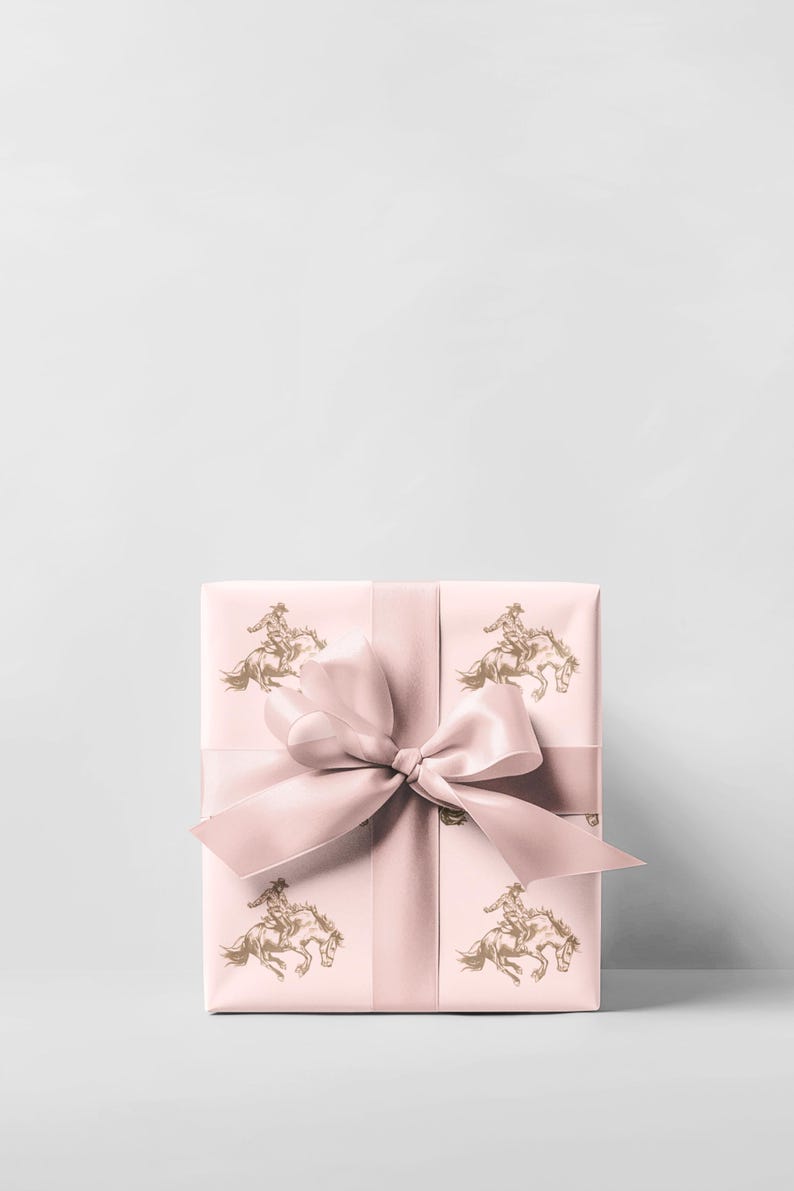 May include: A wrapped gift box with a light pink background and a matching ribbon tied in a bow. The wrapping paper features a repeating pattern of a cowboy riding a horse in a gold color.