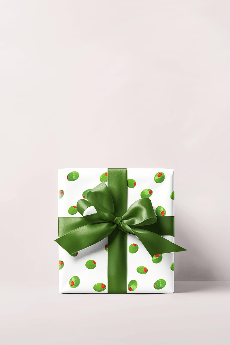 May include: A wrapped gift with white paper featuring a pattern of green olives with red centers. A large, dark green satin ribbon is tied around the package in a bow.