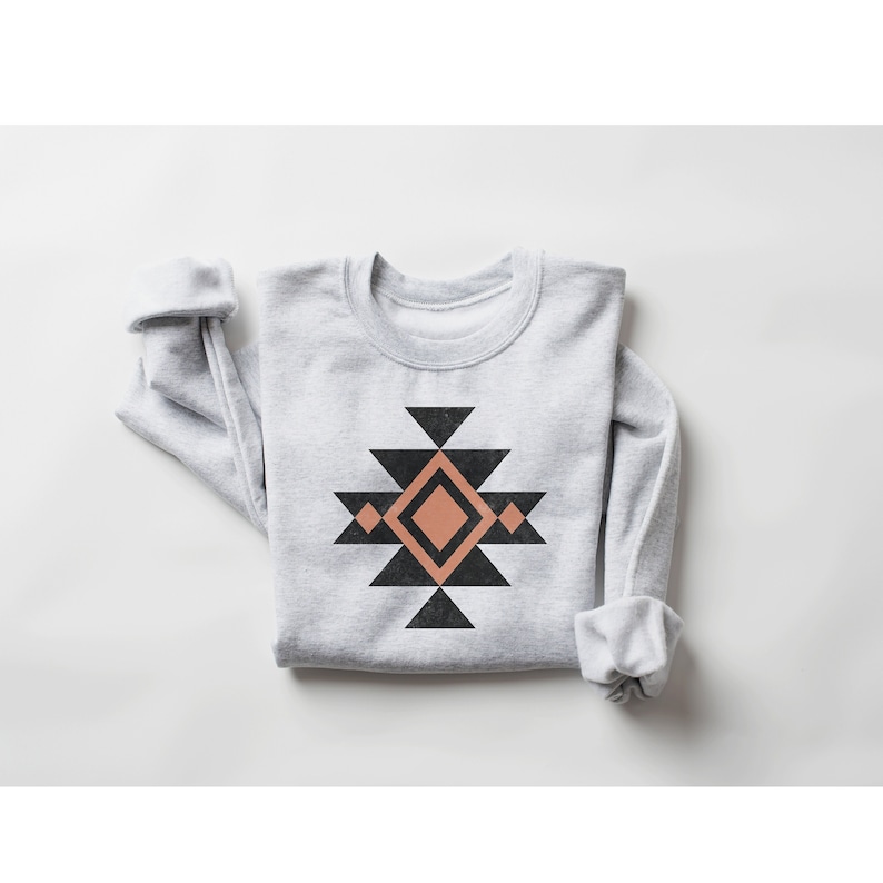 May include: A grey sweatshirt with a geometric design in black and peach. The design features a large diamond shape with smaller triangles surrounding it.