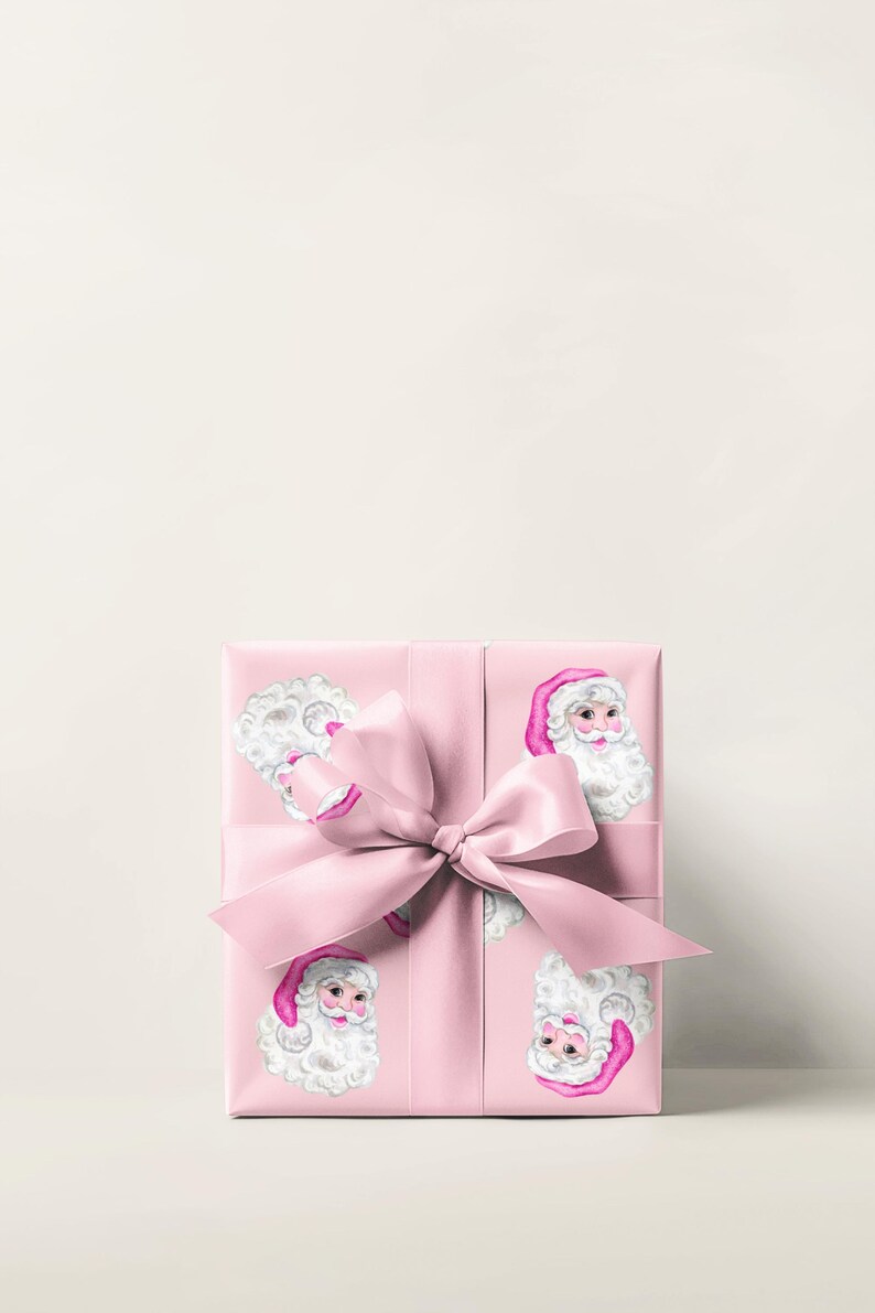 Puede incluir: Una caja de regalo rosa envuelta en papel con ilustraciones de Pap&aacute; Noel. La caja est&aacute; atada con una cinta y un lazo rosas a juego. Las ilustraciones de Pap&aacute; Noel tienen barbas blancas y gorros rosas.