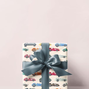 May include: A wrapped gift box featuring a cream-colored paper with a pattern of vintage race cars in various colors. The box is tied with a large, teal-colored satin ribbon and bow, creating a festive presentation.