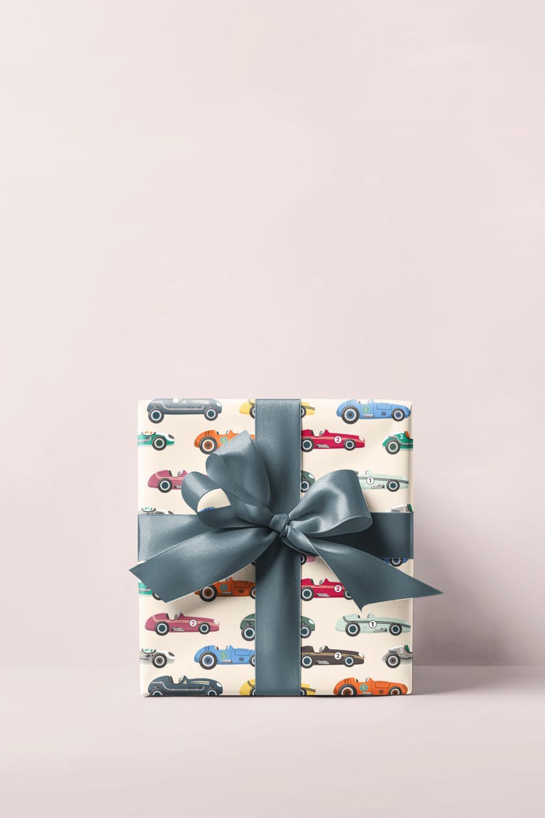 May include: A wrapped gift box featuring a cream-colored paper with a pattern of vintage race cars in various colors. The box is tied with a large, teal-colored satin ribbon and bow, creating a festive presentation.