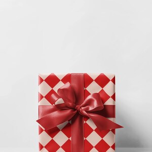 K&ouml;nnte beinhalten: Eine quadratische Geschenkbox, verpackt in Papier mit einem rot-cremefarbenen Rautenmuster. Ein breites, rotes Satinband ist um die Box gebunden und bildet oben eine gro&szlig;e Schleife. Der Hintergrund ist schlicht wei&szlig;.