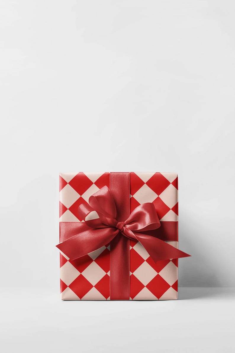 K&ouml;nnte beinhalten: Eine quadratische Geschenkbox, verpackt in Papier mit einem rot-cremefarbenen Rautenmuster. Ein breites, rotes Satinband ist um die Box gebunden und bildet oben eine gro&szlig;e Schleife. Der Hintergrund ist schlicht wei&szlig;.