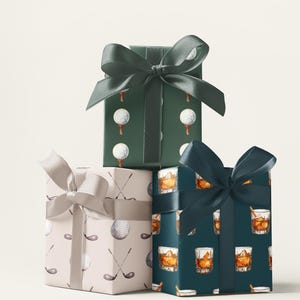K&ouml;nnte beinhalten: Drei verpackte Geschenkboxen mit dekorativen Schleifen. Die Boxen sind in gemustertes Papier mit Golfb&auml;llen, Golfschl&auml;gern und Whiskeygl&auml;sern verpackt. Die Schleifen sind in Gr&uuml;n- und Silbert&ouml;nen gehalten.