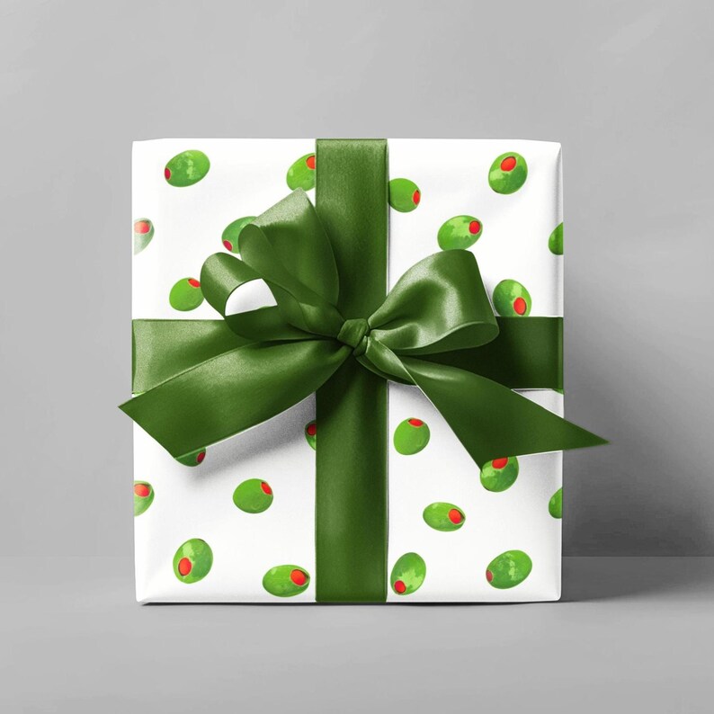 May include: A wrapped gift with white paper featuring a pattern of green olives with red centers. The gift is tied with a dark green satin ribbon and bow, creating a festive presentation.