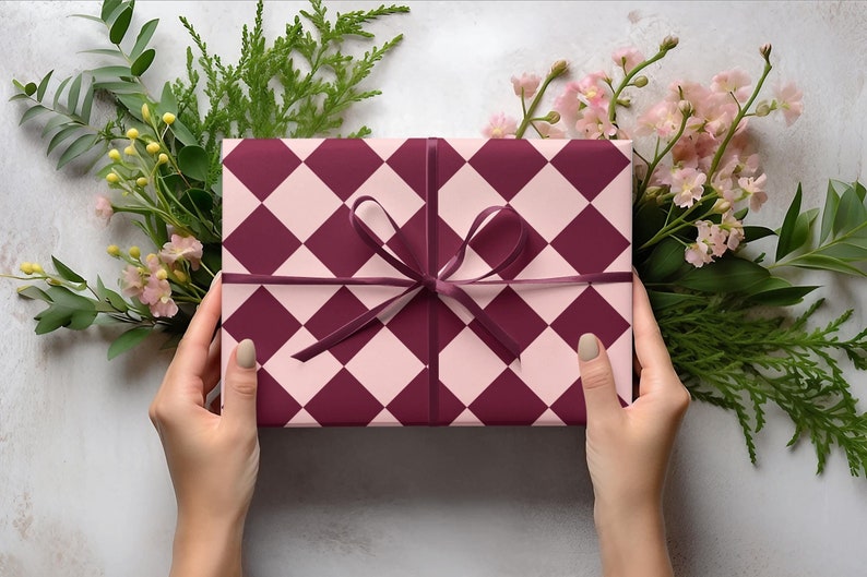 K&ouml;nnte beinhalten: Eine Geschenkbox, verpackt in pink- und burgunderfarbenem kariertem Papier mit einem burgunderfarbenen Band, das zu einer Schleife gebunden ist.