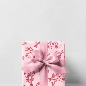 May include: A wrapped gift box with a pink lobster pattern on the wrapping paper. A matching pink satin ribbon is tied in a bow around the box. The background is a plain white.
