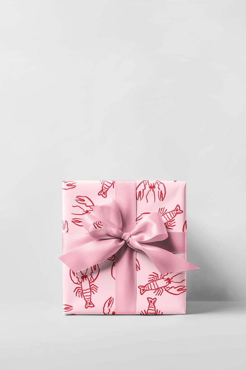 May include: A wrapped gift box with a pink lobster pattern on the wrapping paper. A matching pink satin ribbon is tied in a bow around the box. The background is a plain white.
