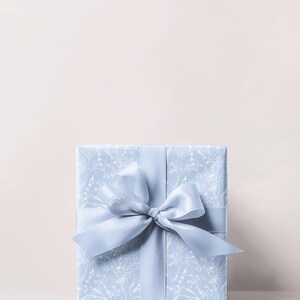Puede incluir: Una caja de regalo azul claro con un patr&oacute;n floral blanco y una cinta de sat&eacute;n azul claro a juego atada en un lazo.