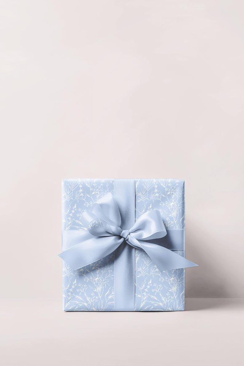 Puede incluir: Una caja de regalo azul claro con un patr&oacute;n floral blanco y una cinta de sat&eacute;n azul claro a juego atada en un lazo.