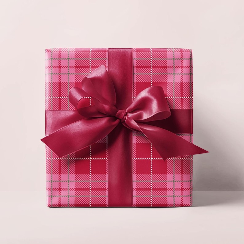 May include: A wrapped gift box with a red and pink plaid pattern. The box is tied with a deep red satin ribbon and bow. The gift wrap has a classic plaid design with white and green accents.