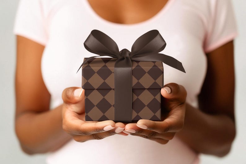 Op de afbeelding: Een persoon houdt een bruin en zwart cadeaudoosje vast met een zwart satijnen lint.