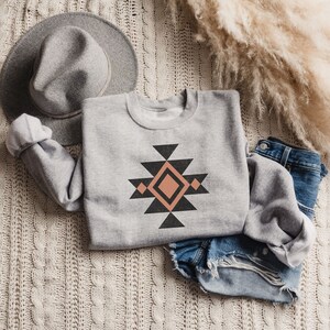 May include: A grey sweatshirt with a geometric design in black and peach. The design features a diamond shape in the centre surrounded by triangles.