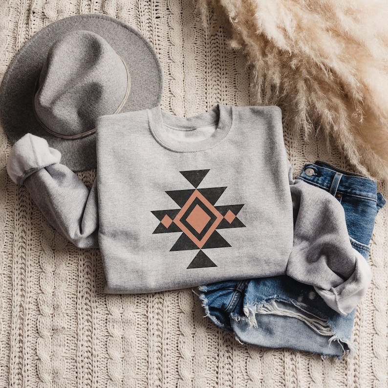 May include: A grey sweatshirt with a geometric design in black and peach. The design features a diamond shape in the centre surrounded by triangles.