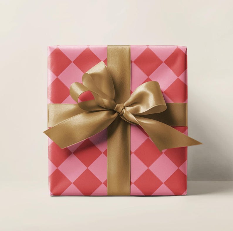 May include: A wrapped gift box with pink and red diamond patterned wrapping paper. A gold satin ribbon is tied around the box in a bow. The gift is ready to be given.